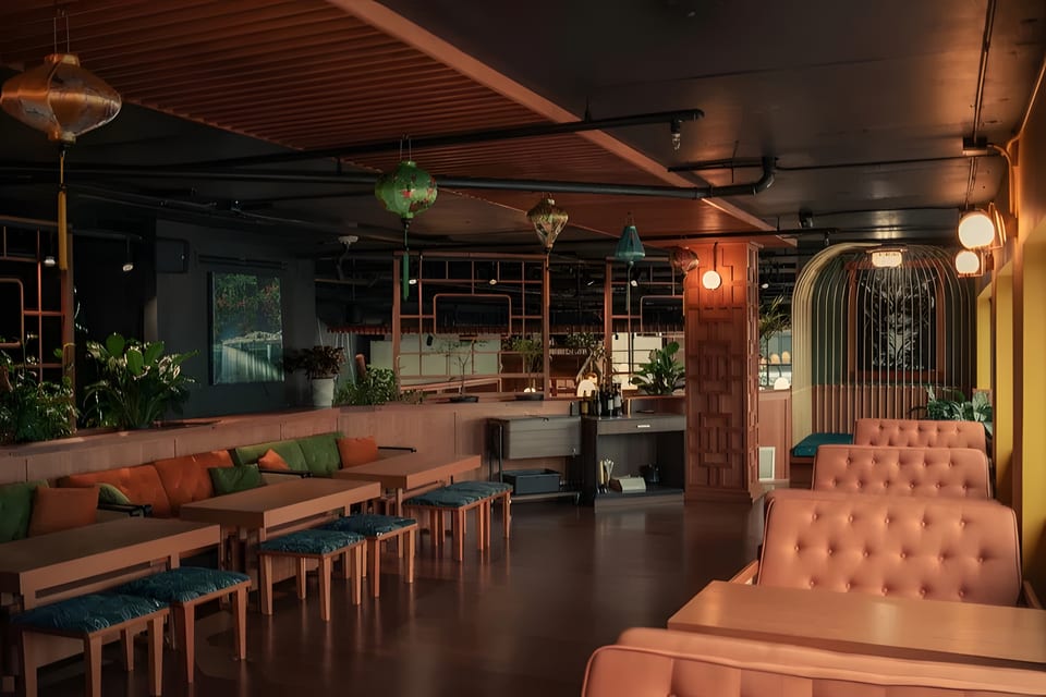 A dimly lit restaurant interior with orange and green seating, wooden tables, and decorative lanterns.