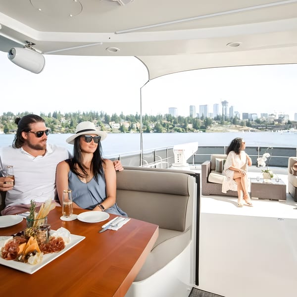 Two couples relaxing on a yacht, enjoying drinks and a charcuterie board with a city skyline view.