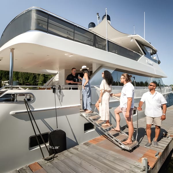 People boarding a large white yacht from a wooden dock on a sunny day.