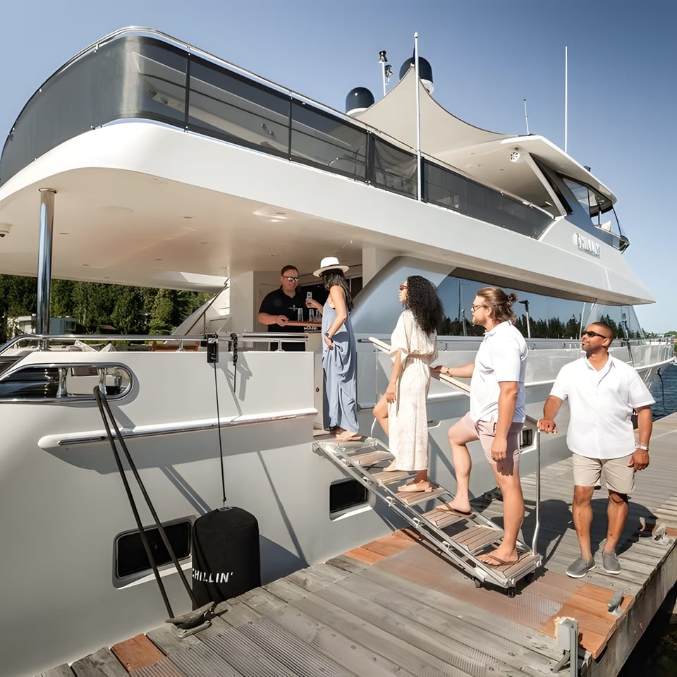 People boarding a large white yacht from a wooden dock on a sunny day.