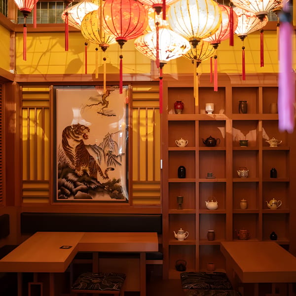 A cozy restaurant interior with wooden tables, benches, a tiger painting, and hanging lanterns.