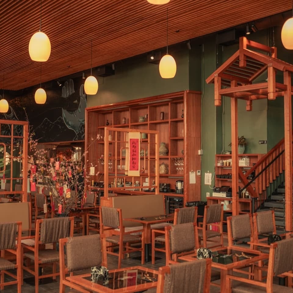 A restaurant interior with wooden furniture, green walls, hanging lights, and a decorative wooden archway.