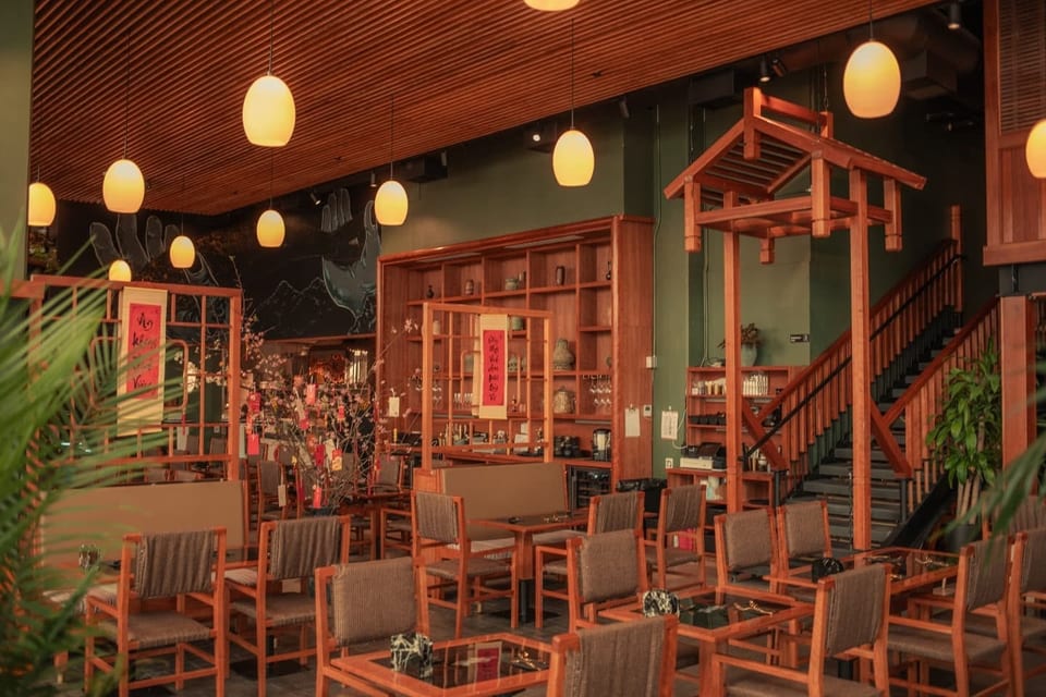 A restaurant interior with wooden furniture, green walls, hanging lights, and a decorative wooden archway.