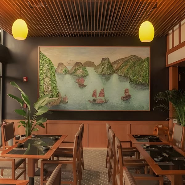 Restaurant interior with wooden tables, chairs, a large mural of boats on water, and yellow pendant lights.