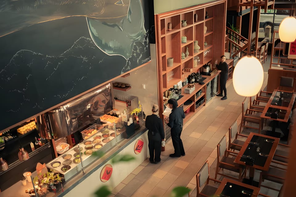 Overhead view of a modern restaurant interior with a food counter, dining tables, and staff.