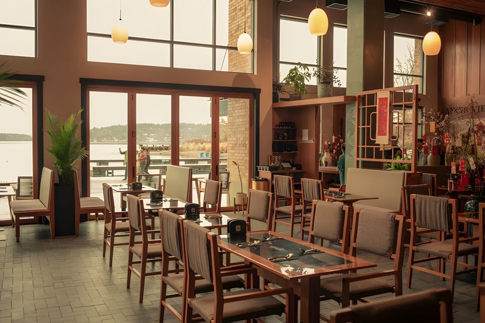 Spacious restaurant dining room with wooden tables and chairs, large windows overlooking a lake.