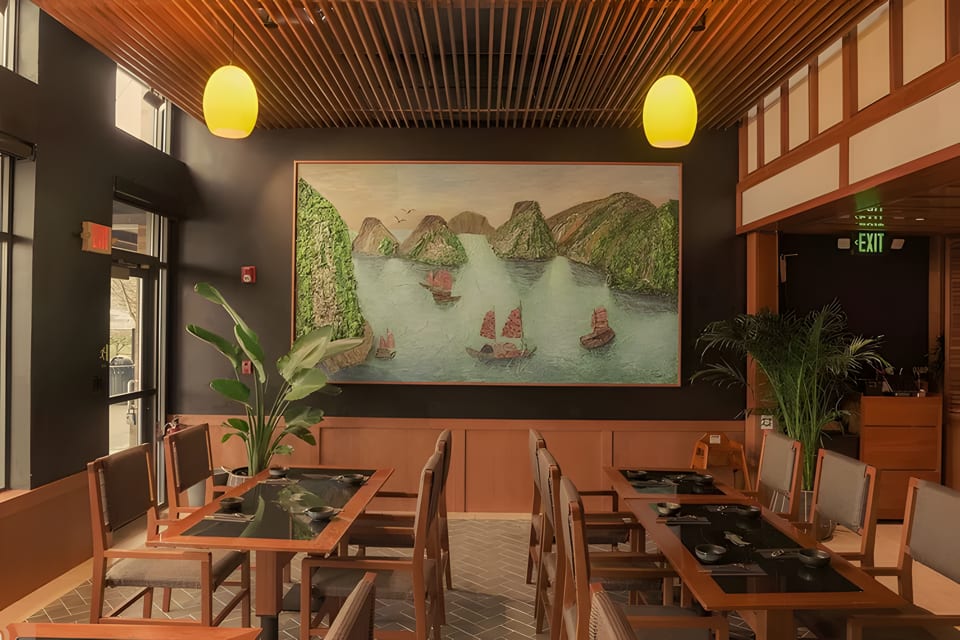 Restaurant interior with dark walls, wooden tables, chairs, and a large painting of boats on water.