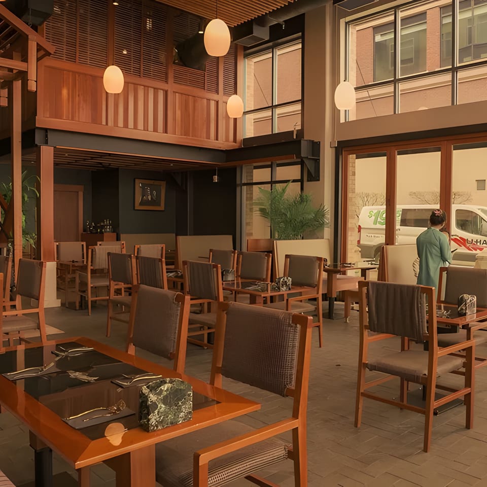 Spacious restaurant interior with wooden tables and chairs, a grand staircase, and large windows.